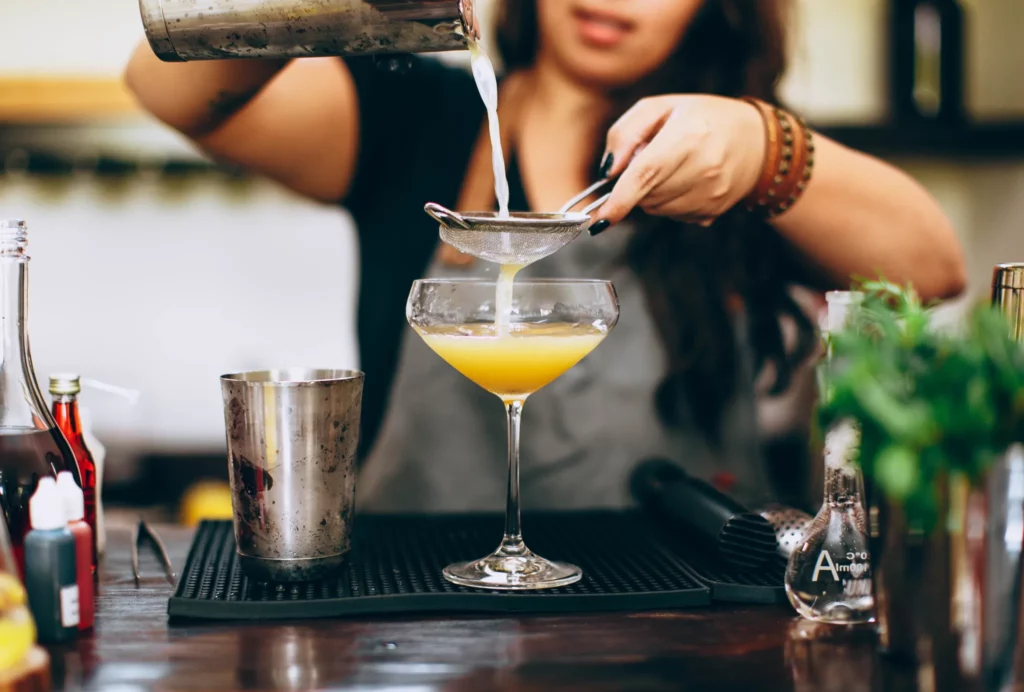 A bartender pours the contents of a cocktail at the bar.