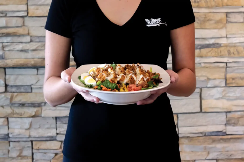 A server presents The Nest Crispy Chicken Cobb Salad on a white plate.